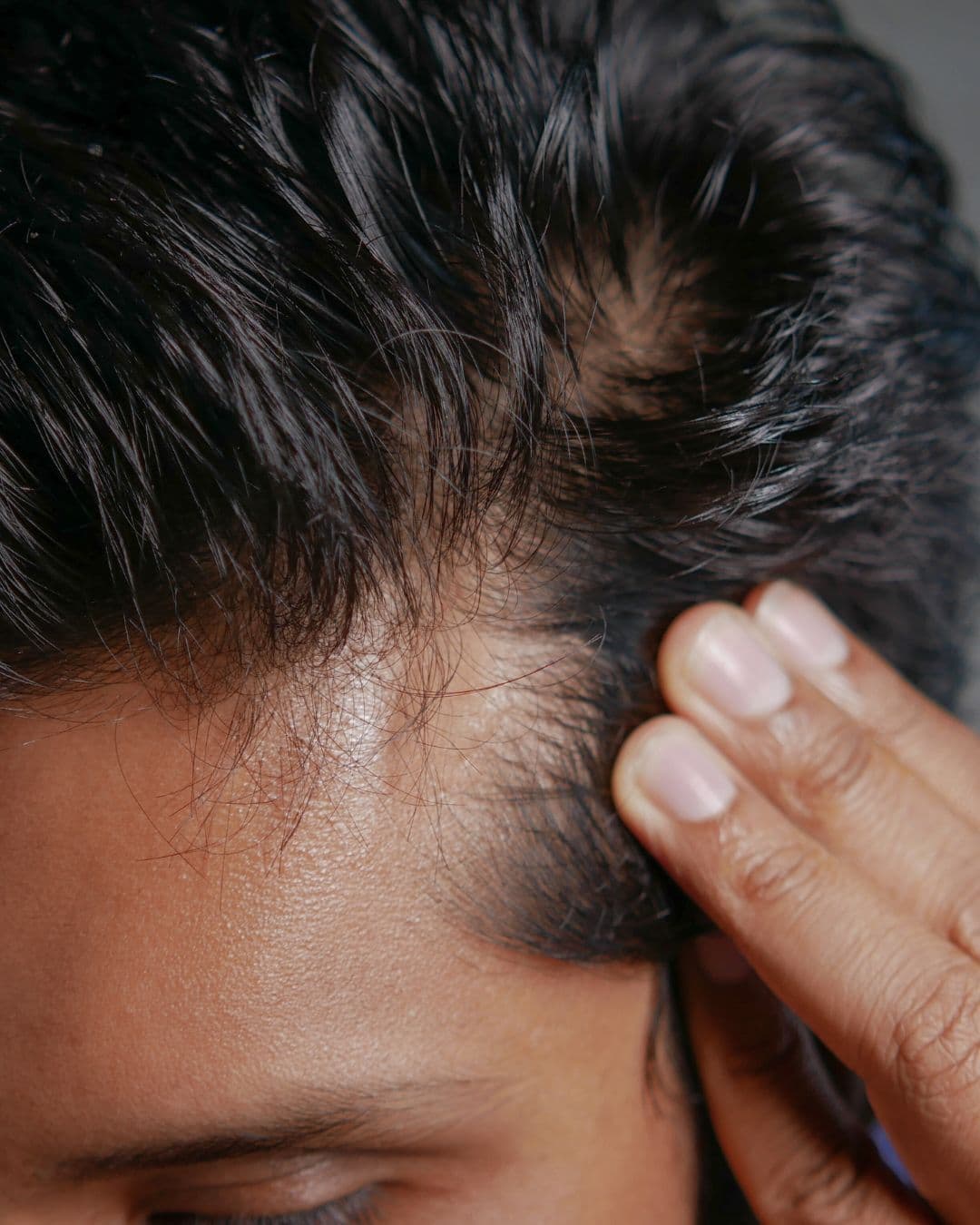 Mann fasst sich ins dunkle Haar, Nahaufnahme Kopf und Hand